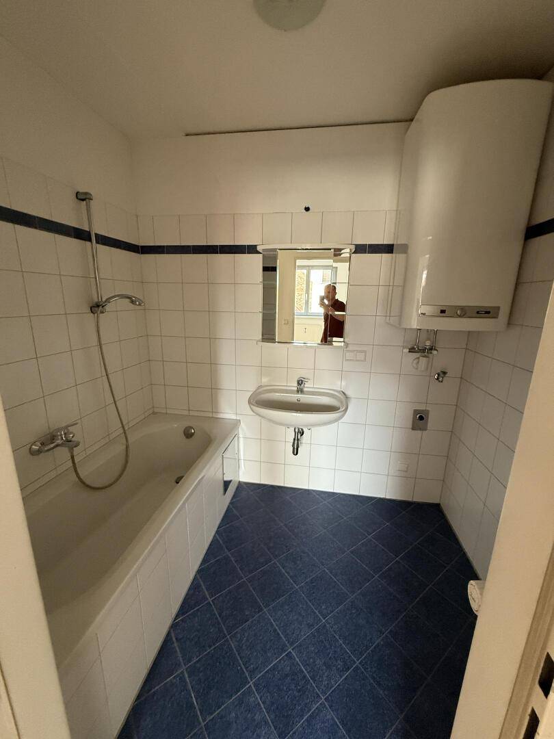 Badezimmer mit Badewanne, Waschbecken, Spiegel und blauen Bodenfliesen.
