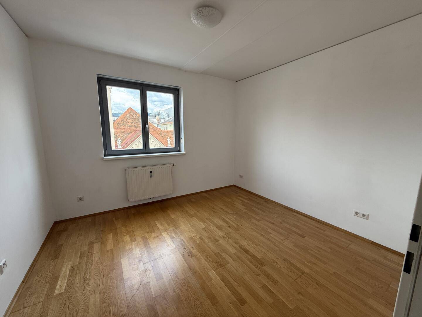 Helles Schlafzimmer mit Parkettboden, weiß gestrichenen Wänden und Fenster.