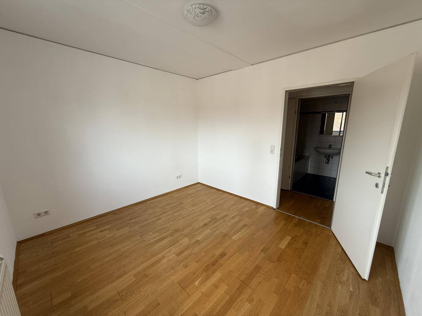 Schlafzimmer mit Parkettboden und Zugang zum Badezimmer, ideal für Privatsphäre.