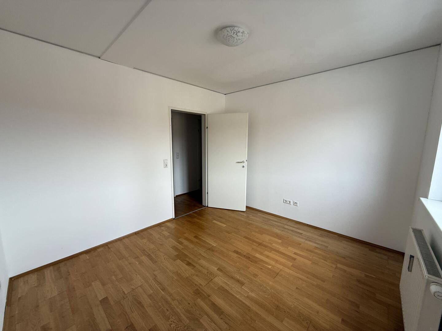 Leeres Schlafzimmer mit Parkettboden und weißen Wänden, bereit zur individuellen Einrichtung.