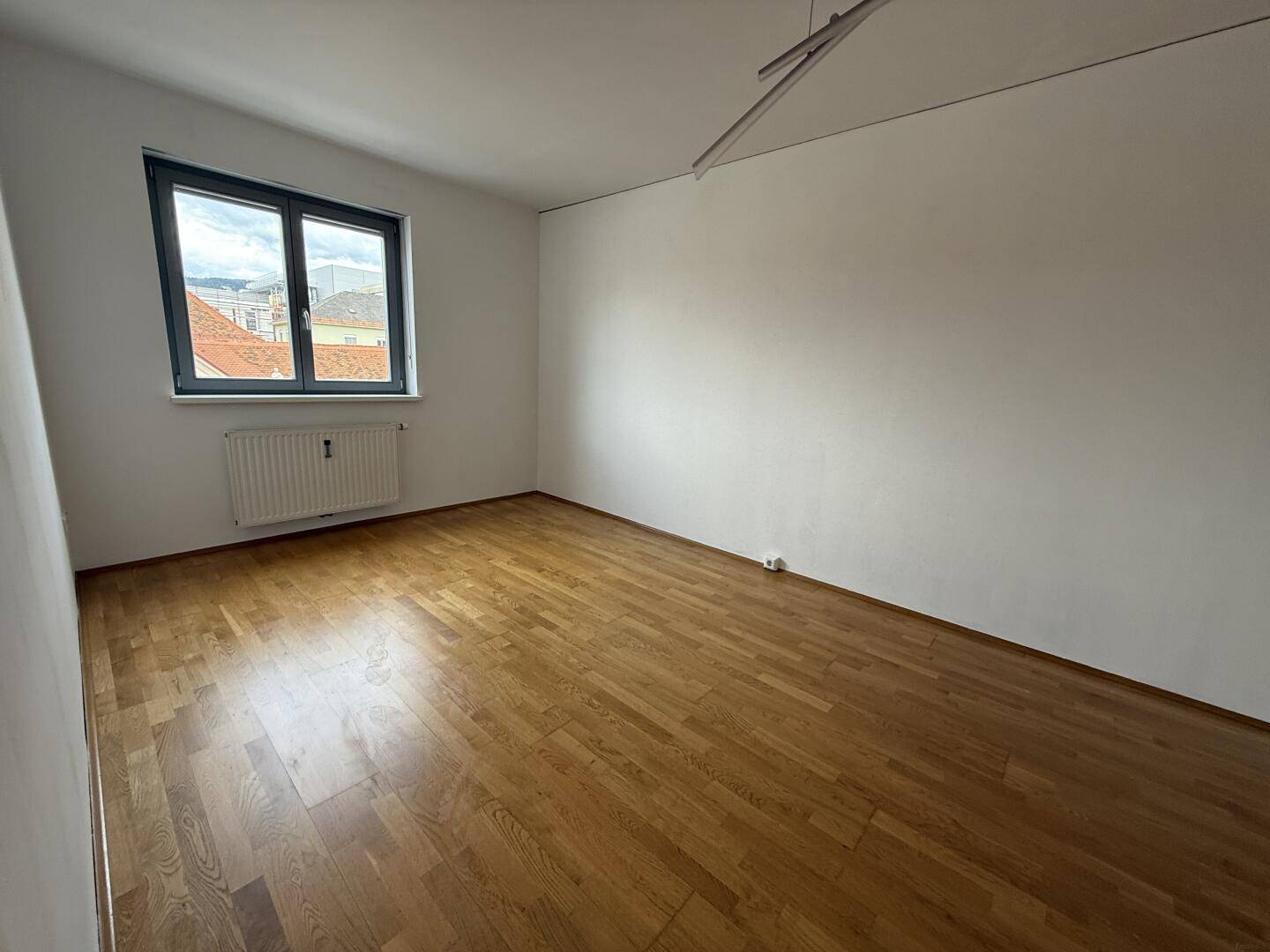 Geräumiges Wohnzimmer mit Parkettboden, weißen Wänden und großem Fenster.