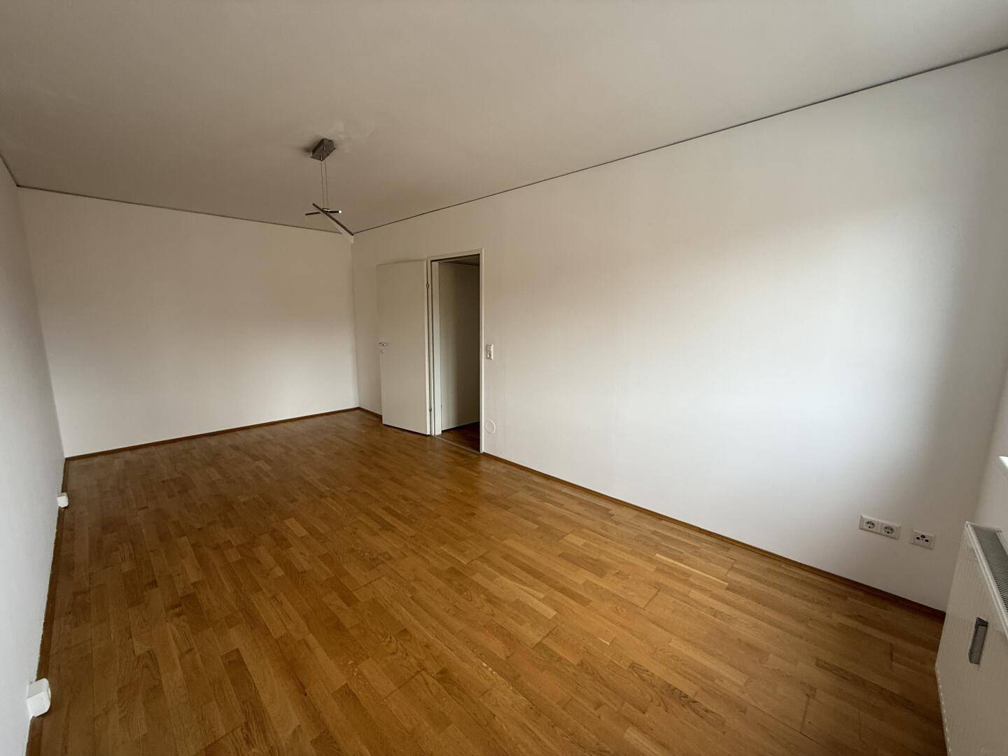 Lichtdurchflutetes Wohnzimmer mit Parkettboden und weißen Wänden, ideal zum Entspannen.
