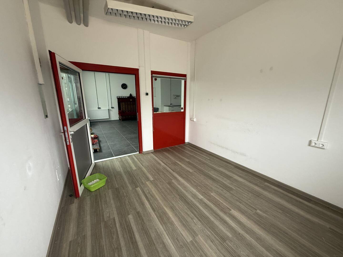 Leerer Gewerberaum mit Laminatboden und roten Türen, bereit zur individuellen Gestaltung.