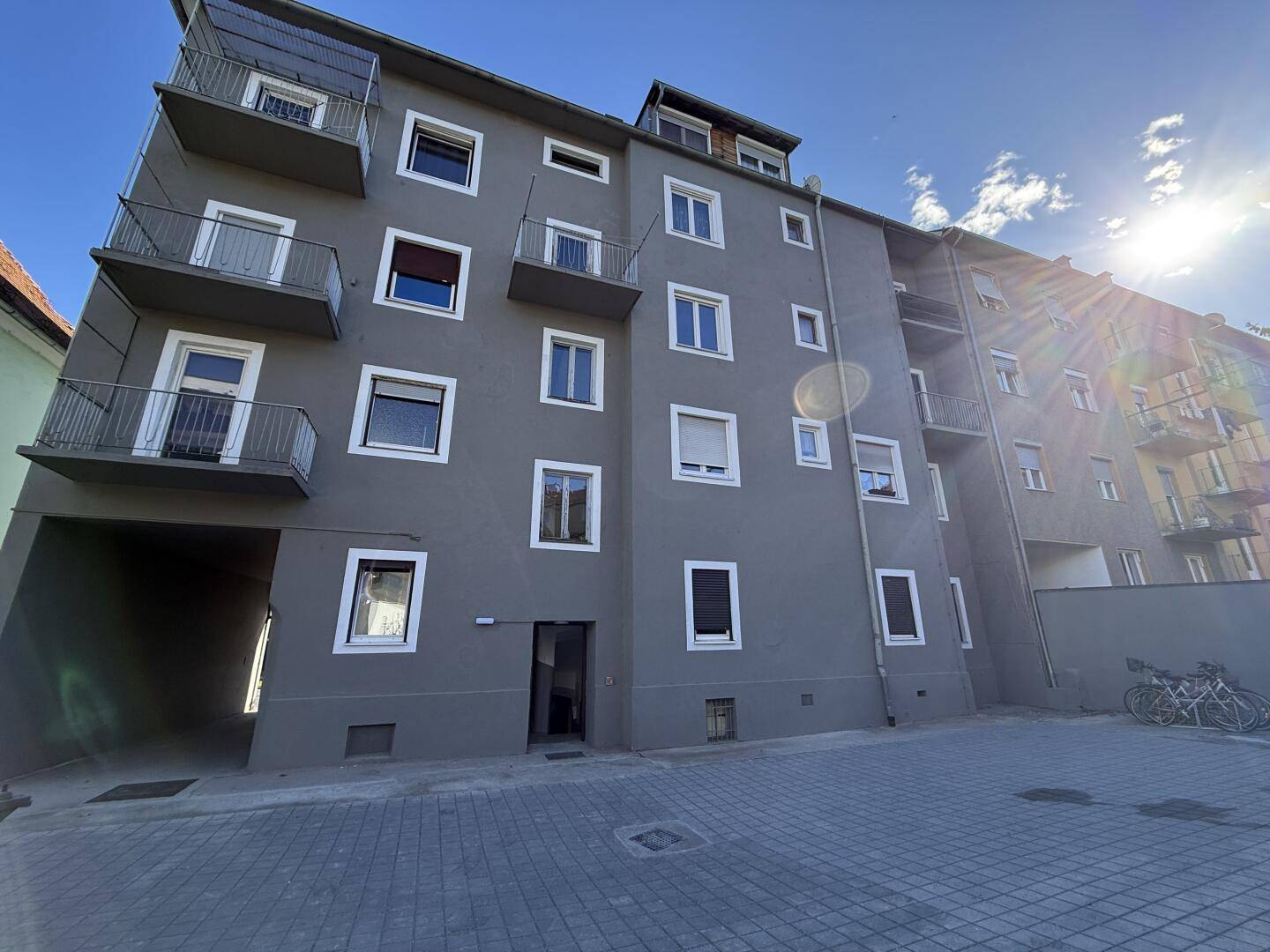 Modernes Mehrfamilienhaus mit grauer Fassade, Balkonen, französischen Balkonen und Parkplatz im Innenhof.