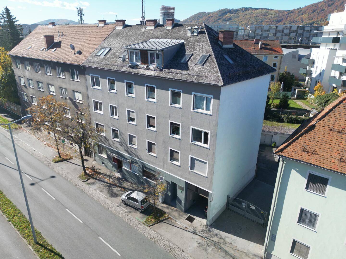 Luftaufnahme eines Mehrfamilienhauses mit grauer Fassade, Satteldach und umliegender Bebauung.