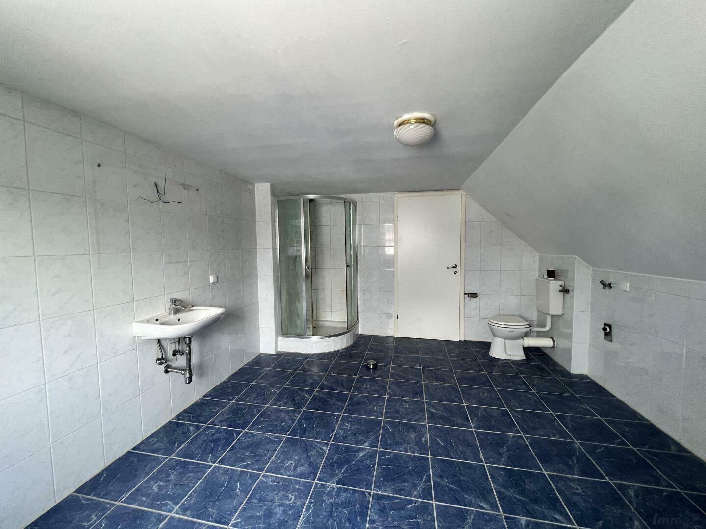 Geräumiges Badezimmer im Dachgeschoss mit blauen Fliesen, Dusche, Waschbecken und Toilette.