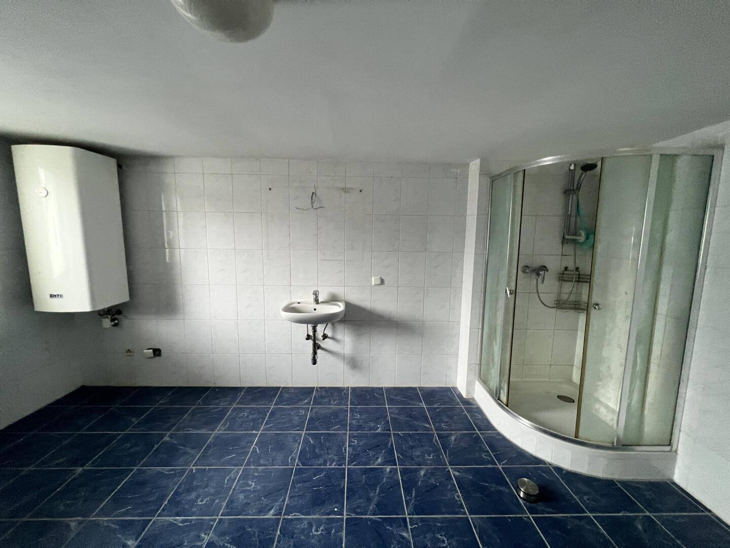 Badezimmer mit Duschkabine, Waschbecken und Boiler, ausgestattet mit blauen Bodenfliesen.