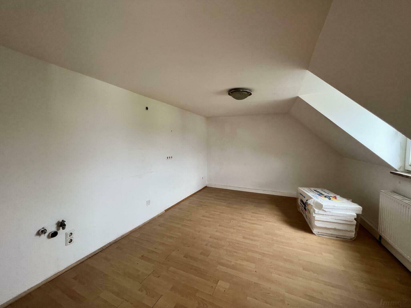 Leeres Zimmer im Dachgeschoss mit Laminatboden und schrägen Wänden, ideal für ein Schlafzimmer.