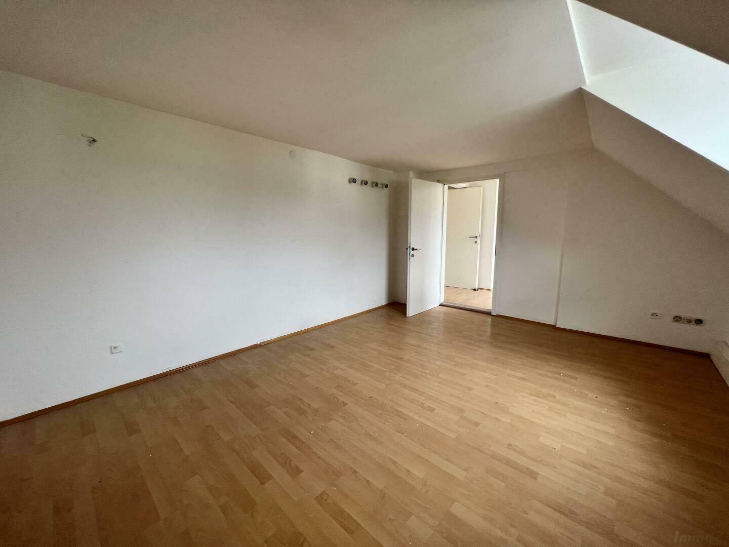 Geräumiges Zimmer im Dachgeschoss mit Laminatboden und Zugang zu weiteren Räumen.