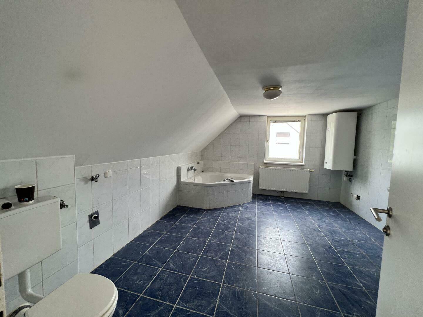 Geräumiges Badezimmer im Dachgeschoss mit blauen Fliesen, Badewanne und Dachschräge.