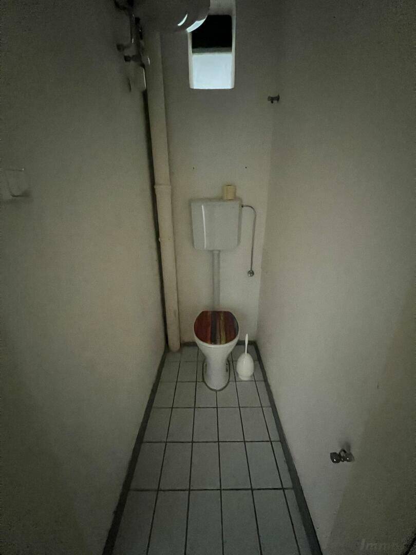 Schmale Gästetoilette mit Fliesenboden und einem einfachen WC mit Spülkasten.