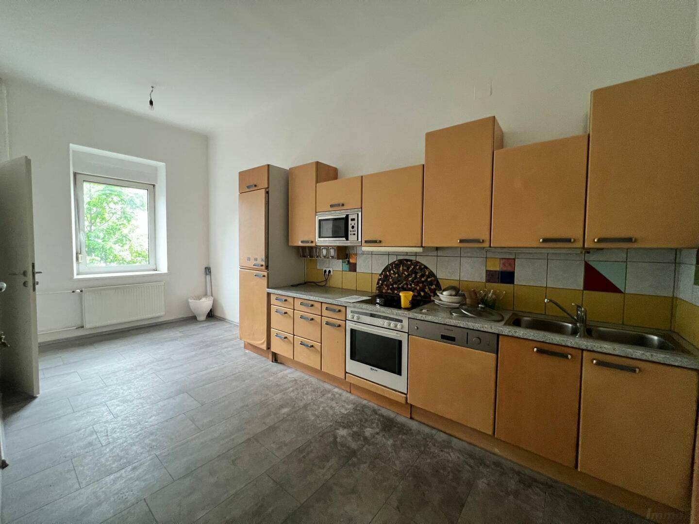Funktionale Einbauküche mit hellbraunen Holzschränken, integrierten Geräten und Fenster.
