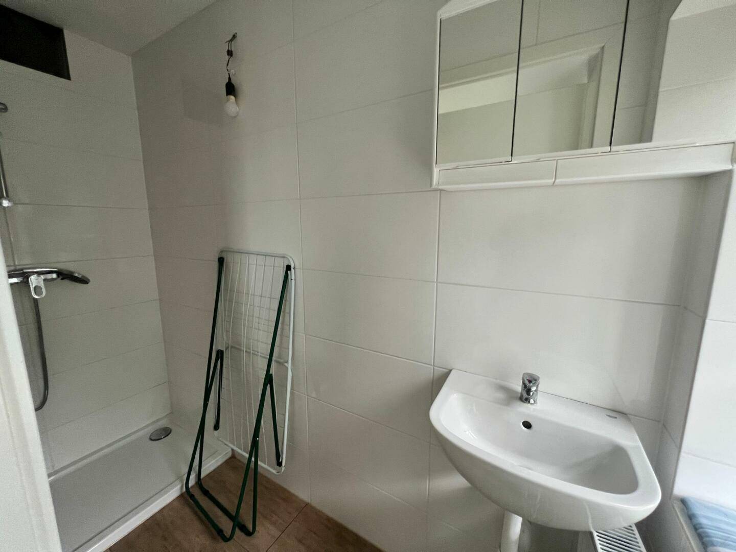 Badezimmer mit weiß gefliesten Wänden, Duschbereich und einem Waschbecken mit Spiegelschrank.