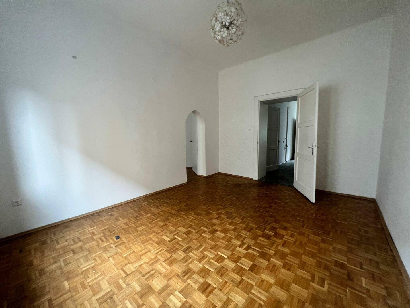 Geräumiges Zimmer mit Parkettboden und Zugang zu weiteren Räumen durch einen eleganten Bogen.