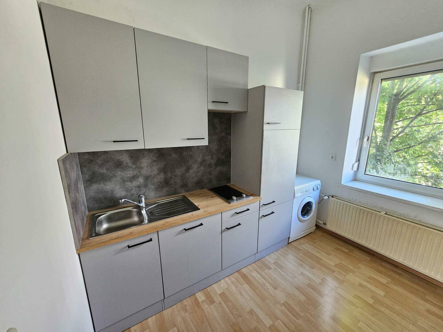 Helle Küchenzeile mit grauen Schränken, Holzarbeitsplatte und Fenster mit Blick ins Grüne.