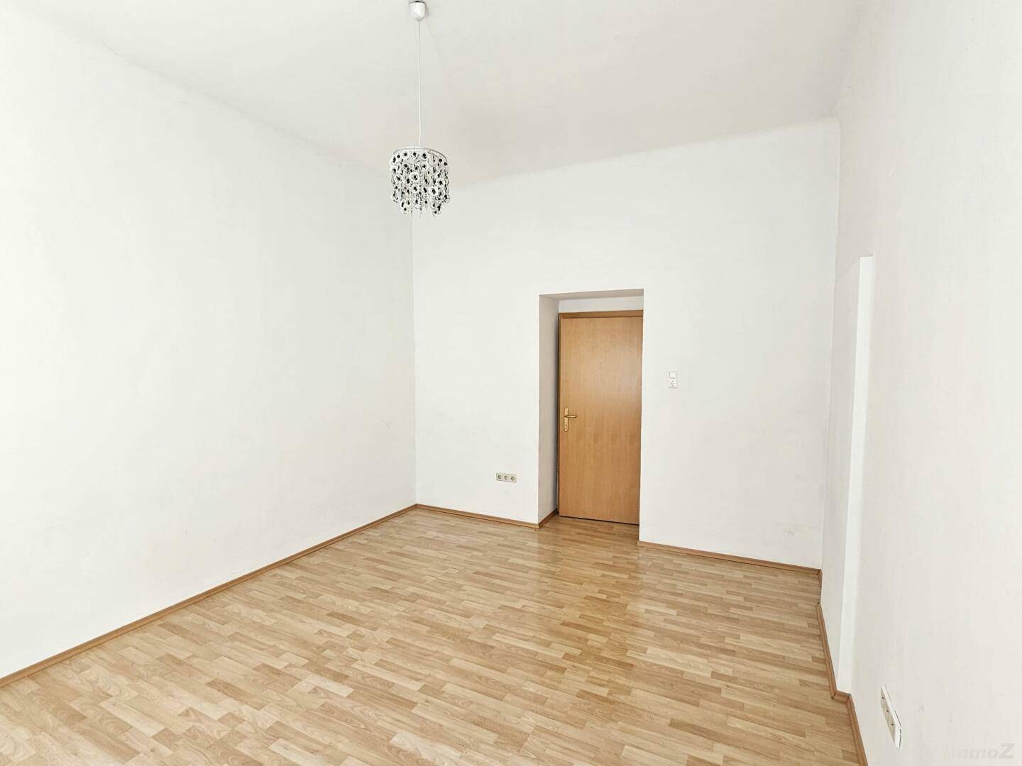 Geräumiges Zimmer mit hellem Parkettboden und weiß gestrichenen Wänden, mit Zugang zu einem weiteren Raum.