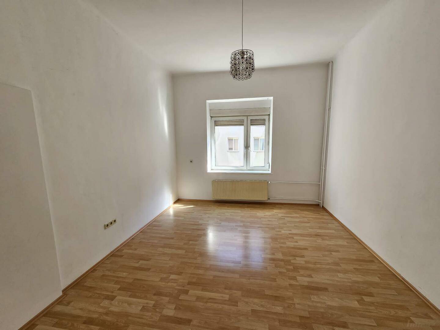 Lichtdurchflutetes Zimmer mit Fenster, Parkettboden und Heizkörper, ideal für Wohnzwecke oder als Schlafzimmer.