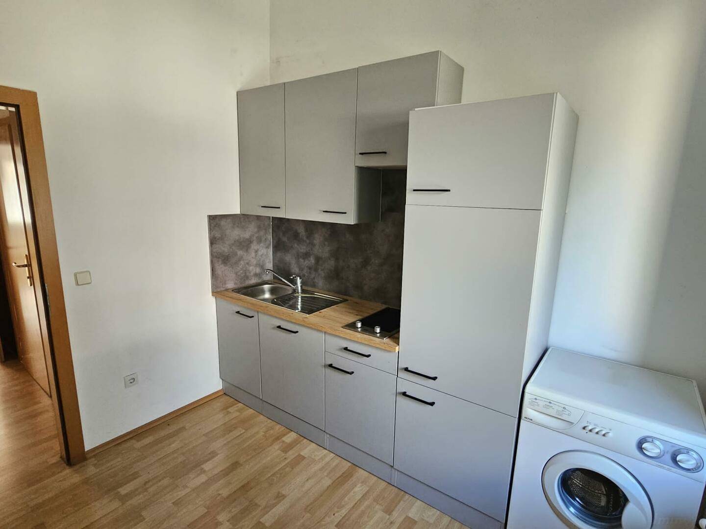 Kompakte Küche mit modernen grauen Fronten, Spüle und Kochfeld, inklusive Waschmaschine.