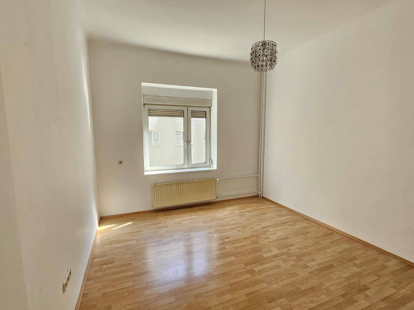 Helles Zimmer mit großem Fenster, Parkettboden und Heizung, ideal für ein Schlaf- oder Arbeitszimmer.