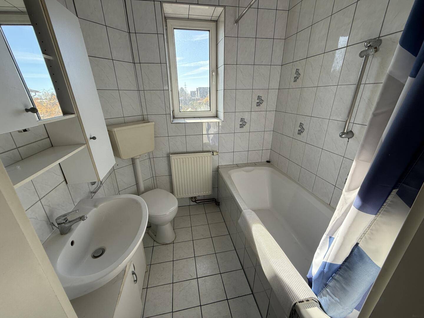 Helles Badezimmer mit Badewanne, WC, Waschbecken und Fenster für natürliche Belüftung.