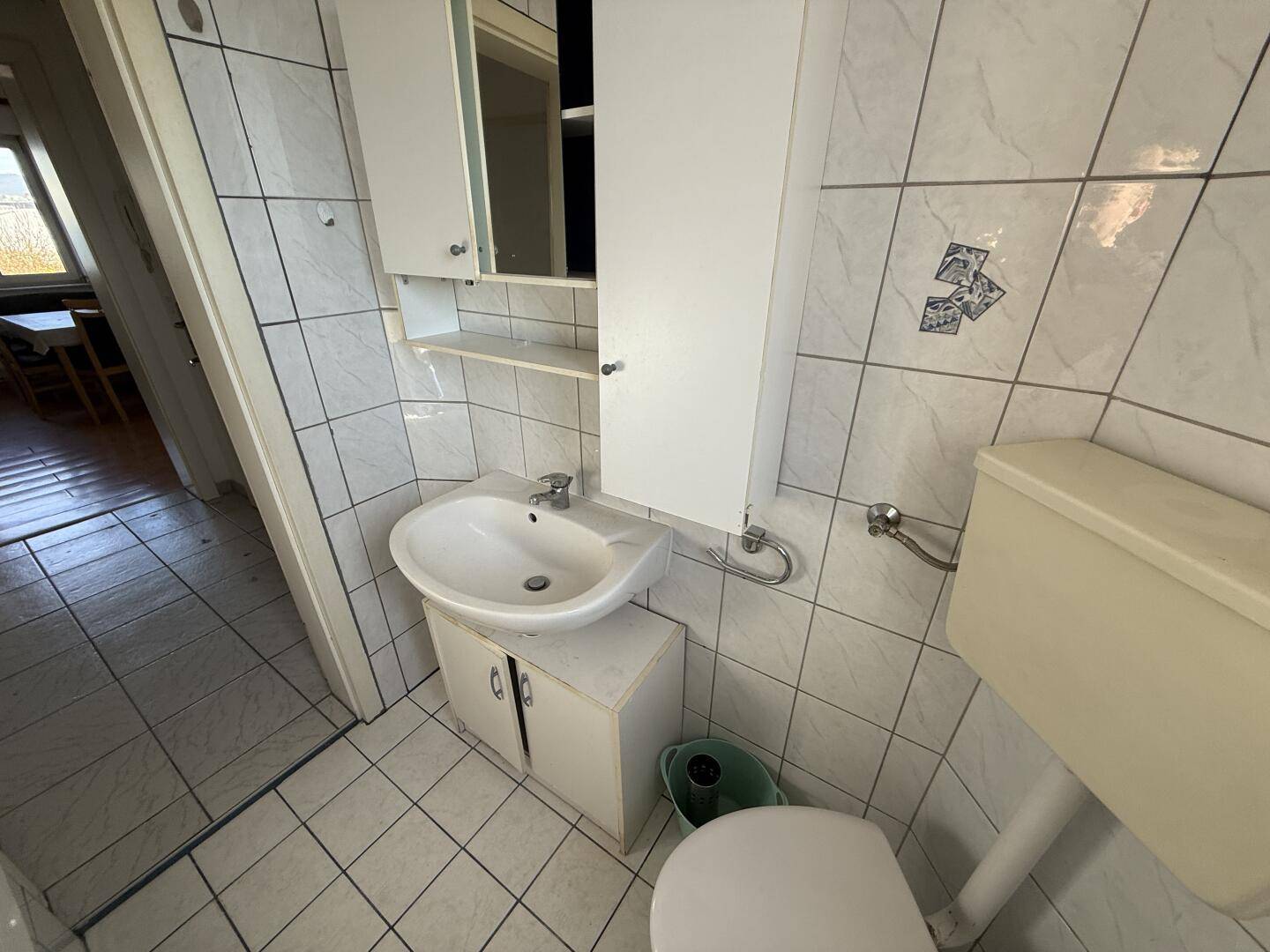 Waschbecken mit Spiegelschrank und WC in einem hell gefliesten Badezimmer.