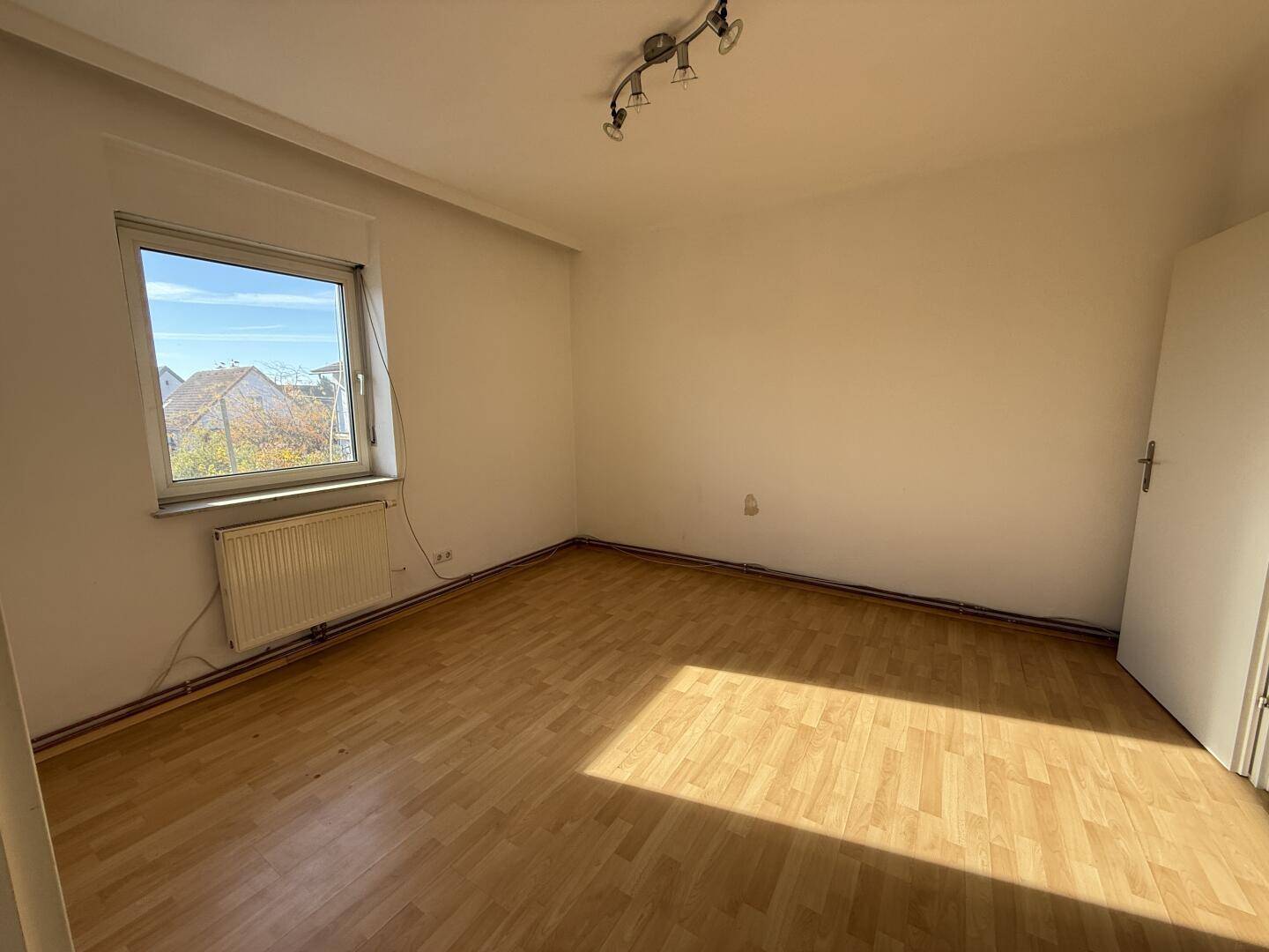 Geräumiges Schlafzimmer mit Parkettboden und großem Fenster, das viel Licht hereinlässt.