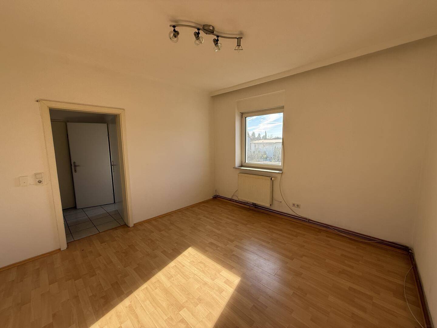 Lichtdurchflutetes Zimmer mit Parkettboden und Heizkörper unter dem Fenster.