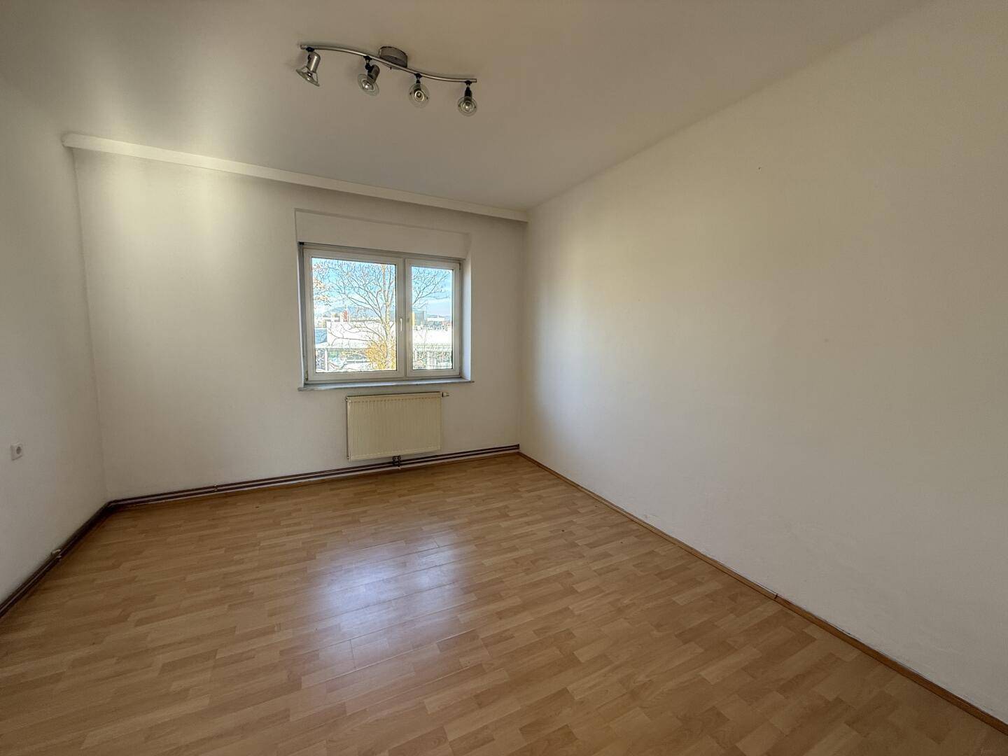 Helles Zimmer mit Parkettboden und Blick ins Grüne durch das Fenster.