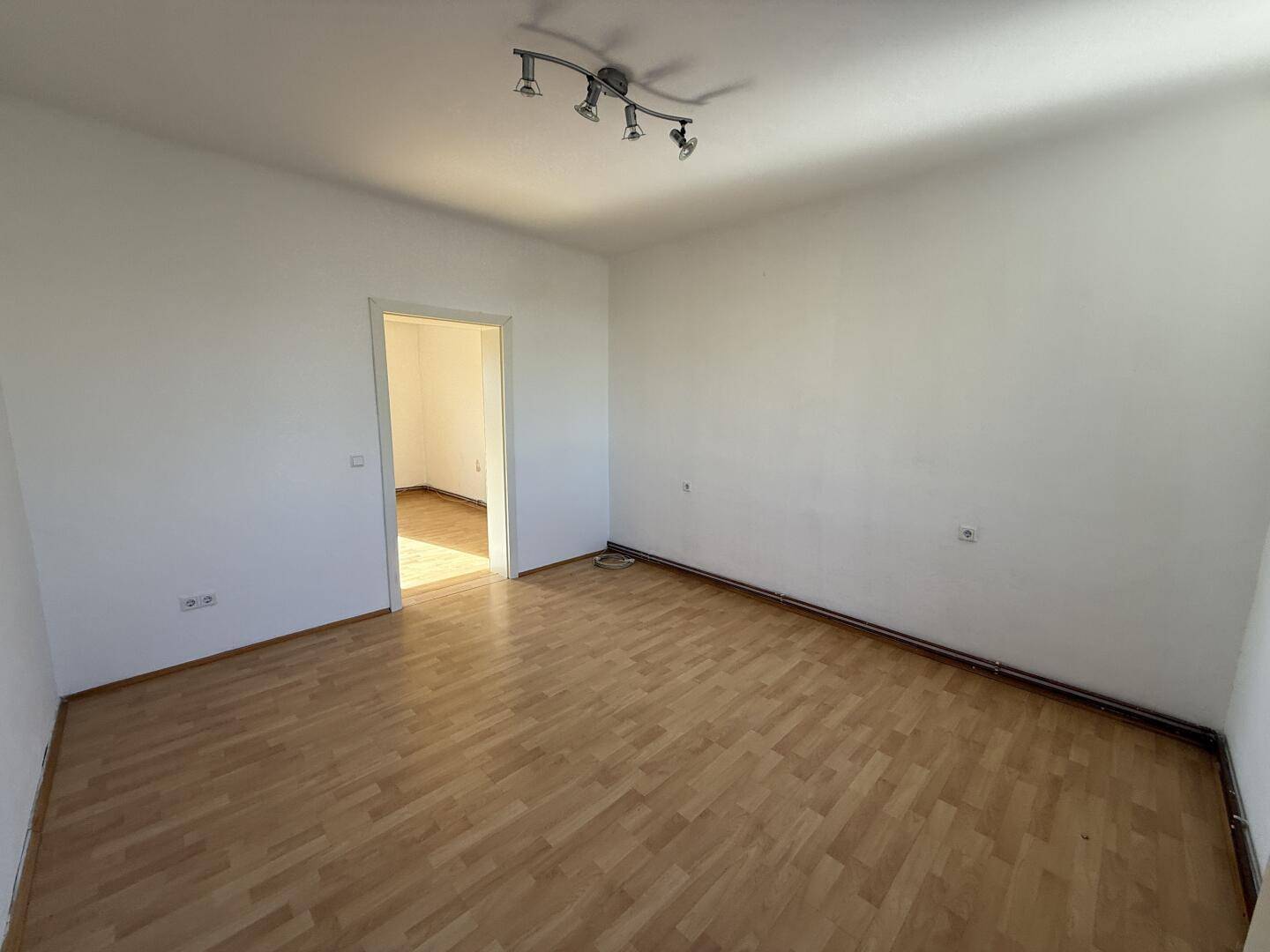 Geräumiges Zimmer mit Parkettboden und Zugang zu einem weiteren Raum.