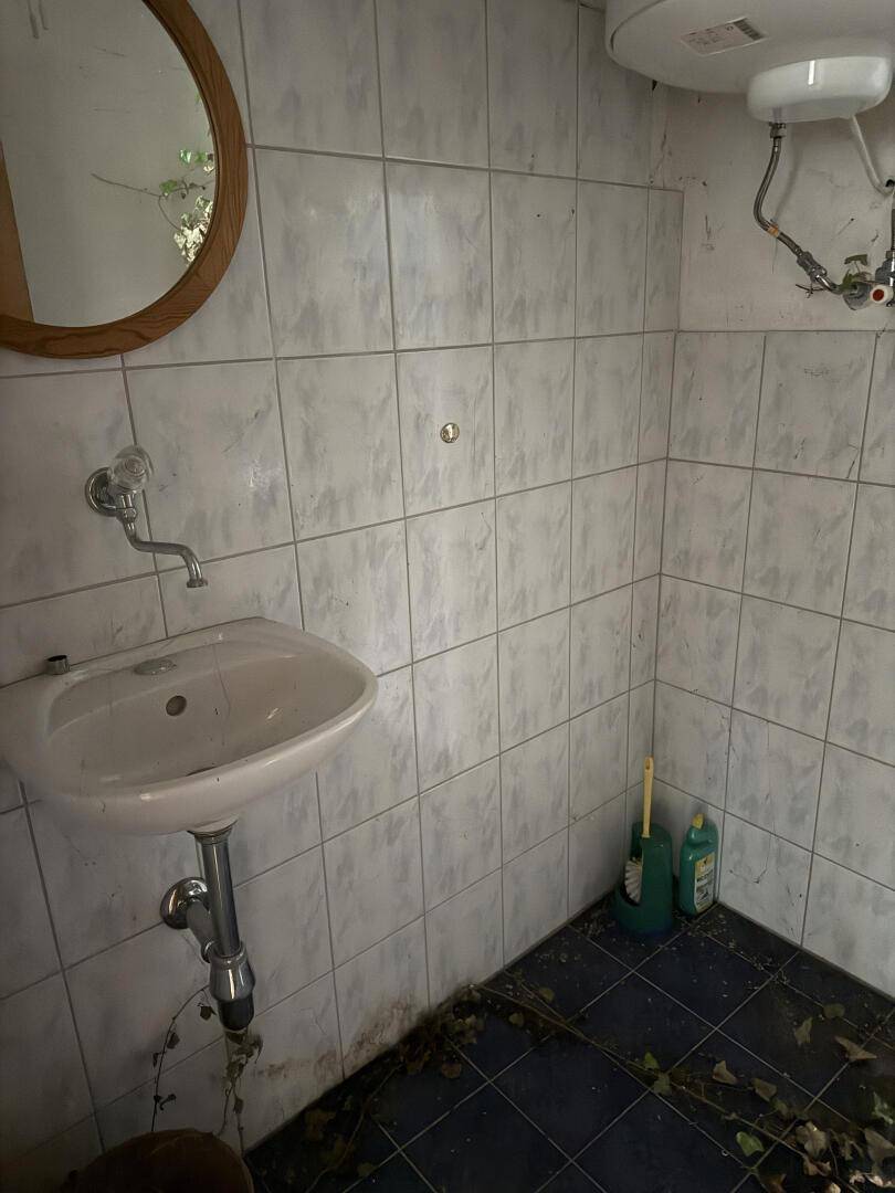 Kleines Badezimmer mit Waschbecken, Spiegel und Fliesen an Wänden und Boden, mit Warmwasserbereiter.