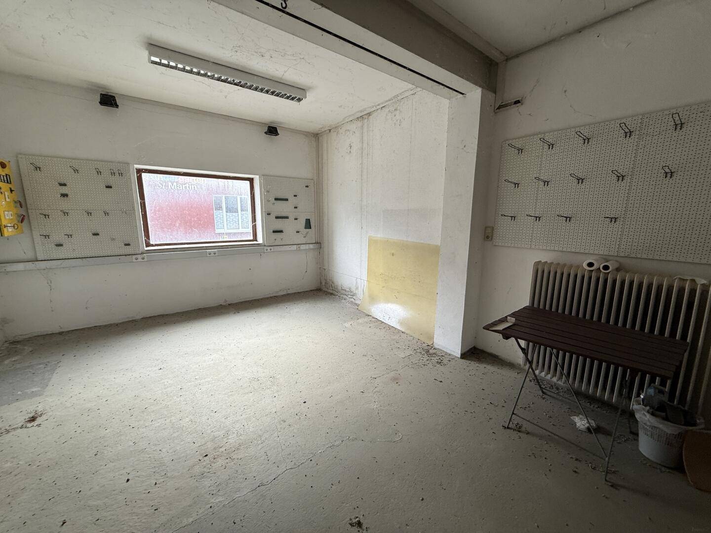 Innenraum mit Betonboden, Fenster und Wänden mit Lochplatten, geeignet als Lager oder Werkstatt.