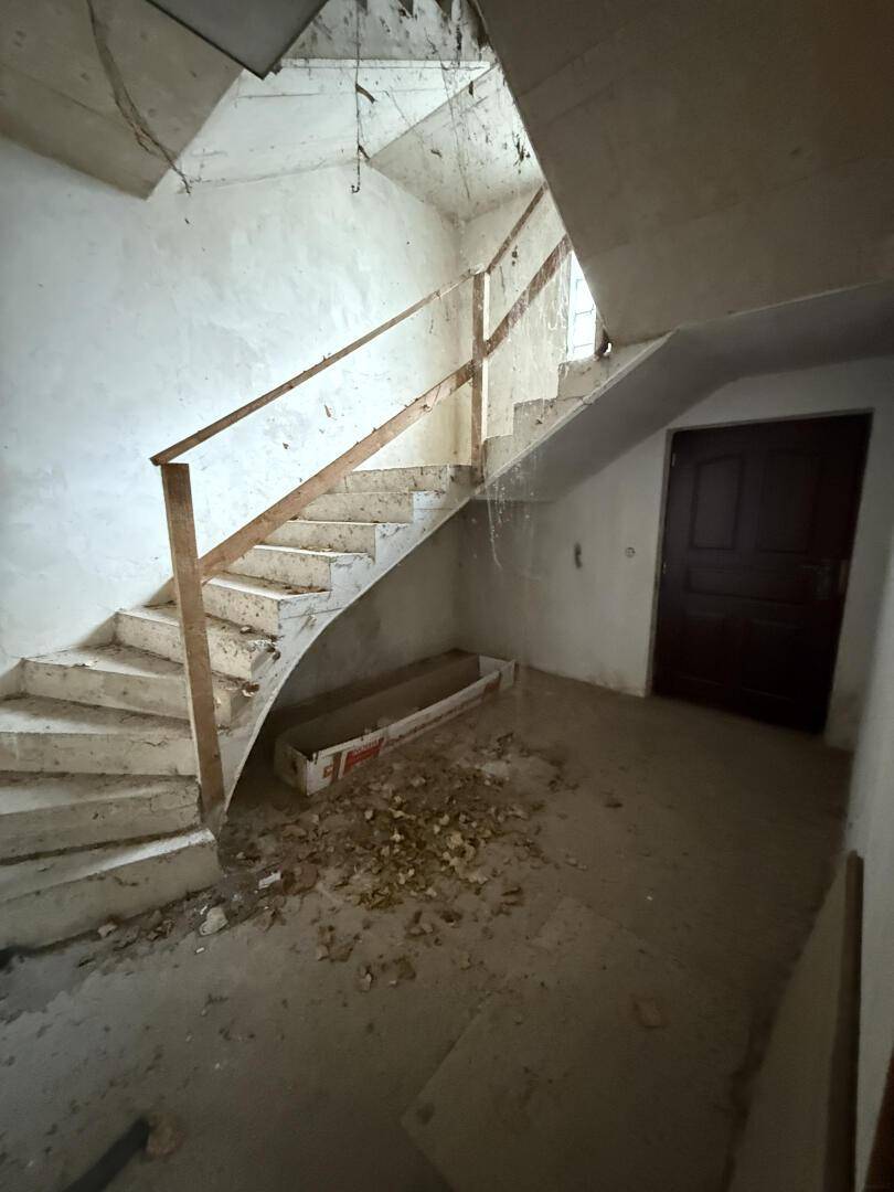Treppenhaus mit Betontreppen und Holzgeländer, in einem Zustand, der Renovierung erfordert.