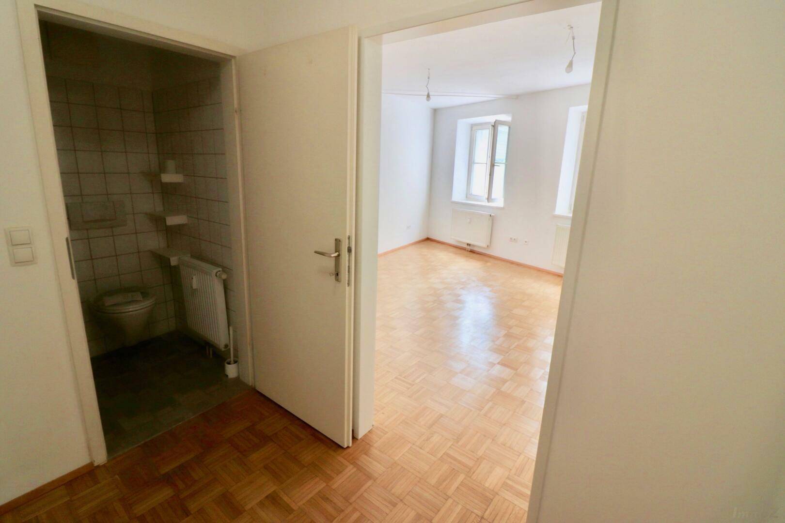 Blick vom Flur in ein helles Zimmer und ein kleines Badezimmer.