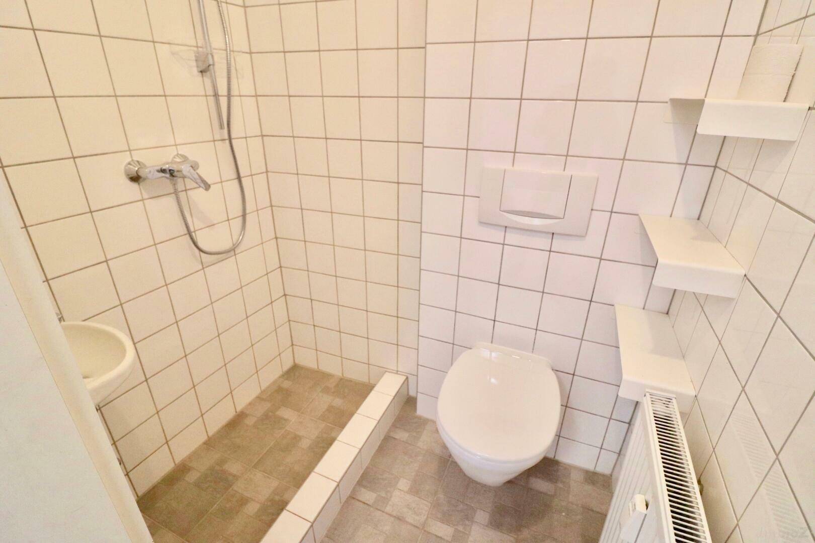 Kleines Badezimmer mit Dusche, WC und weißen Fliesen in gutem Zustand.