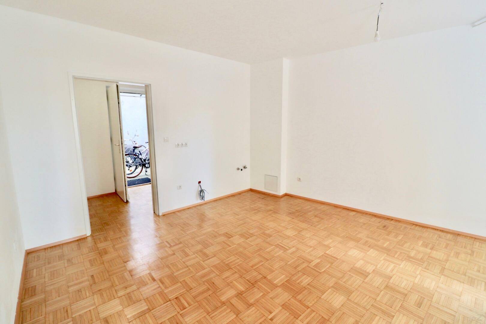 Helles Zimmer mit Parkettboden und Zugang zu einem Außenbereich, ideal für flexible Nutzung.