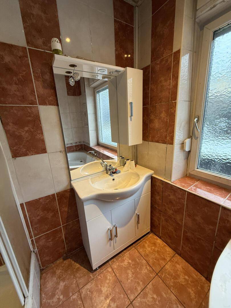 Badezimmer mit braun-beigen Fliesen, Waschbecken, Spiegelschrank und Fenster.