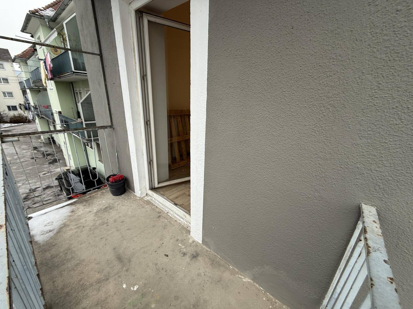 Betonbalkon mit Blick auf benachbarte Gebäude und einfacher Metallbrüstung.