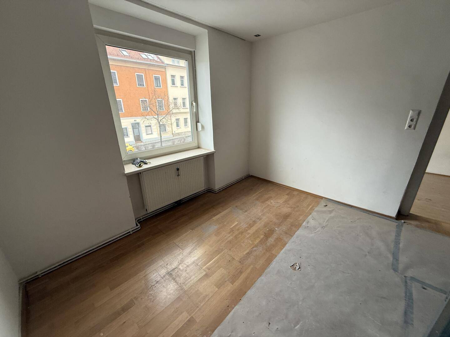 Heller Raum im Bauzustand mit Holzboden und Blick auf die Straße durch das Fenster.