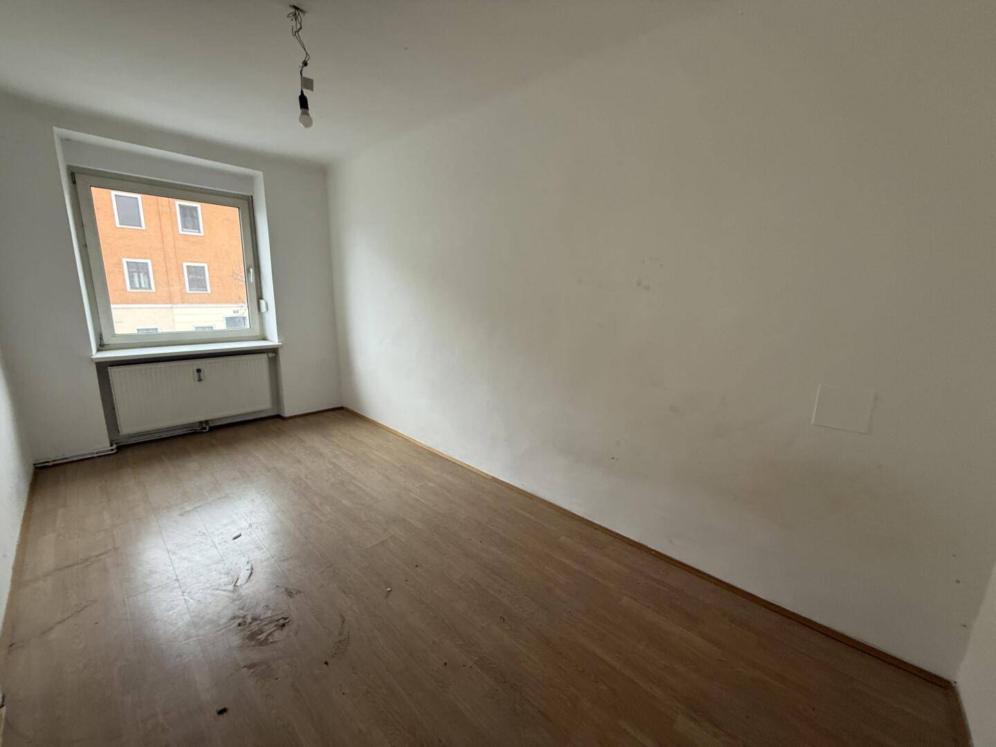 Leerer Raum mit Holzboden, weiß gestrichenen Wänden und Fenster.