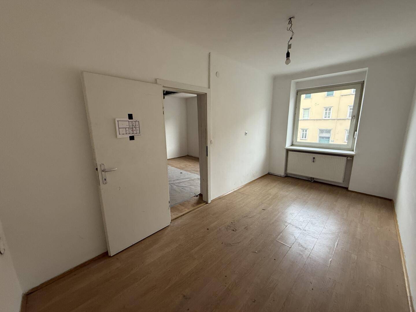 Heller, leerer Raum mit Holzboden, weißer Tür und Fenster.