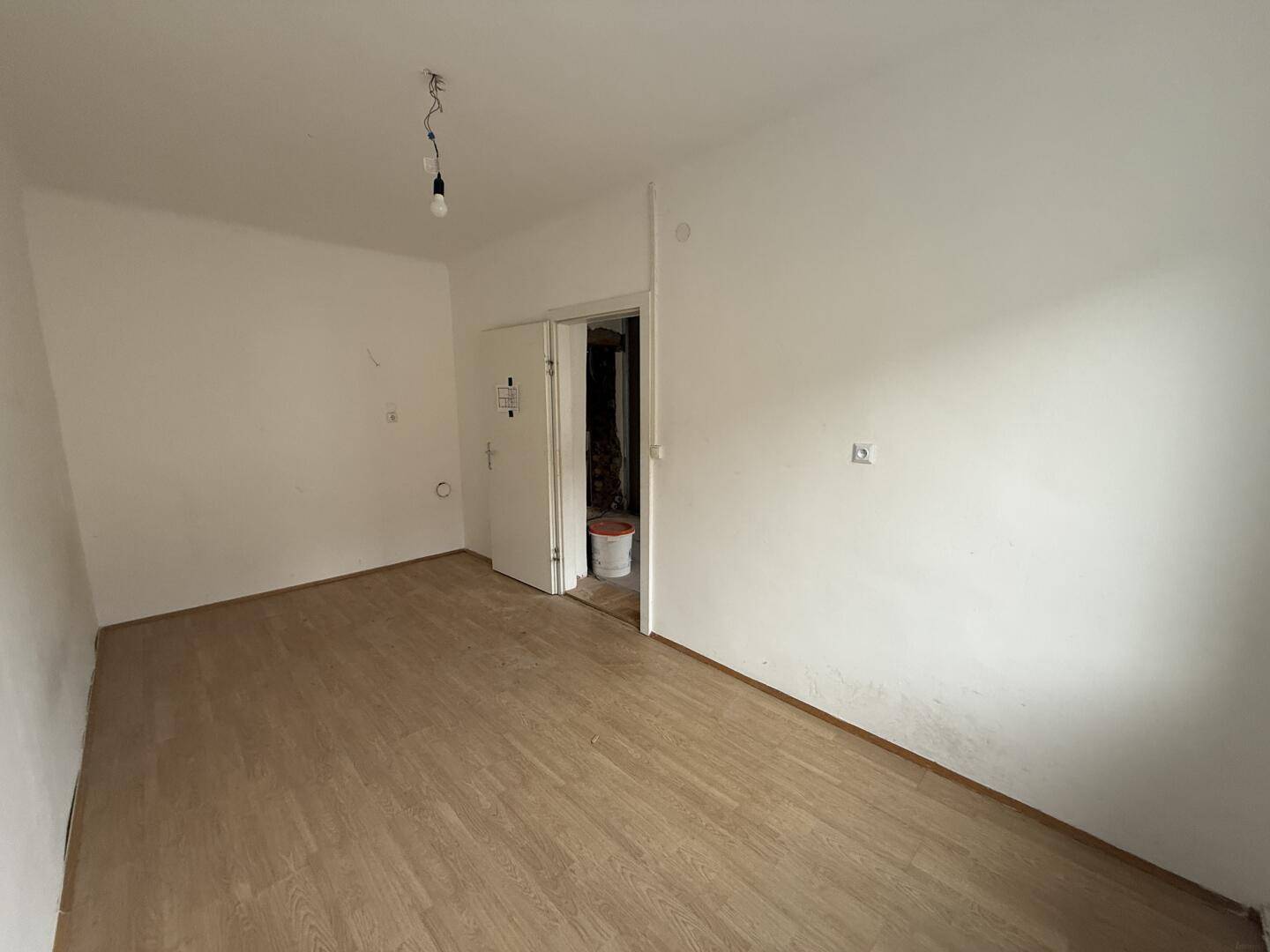 Leerer Raum mit Holzboden, weiß gestrichenen Wänden und offener Tür.