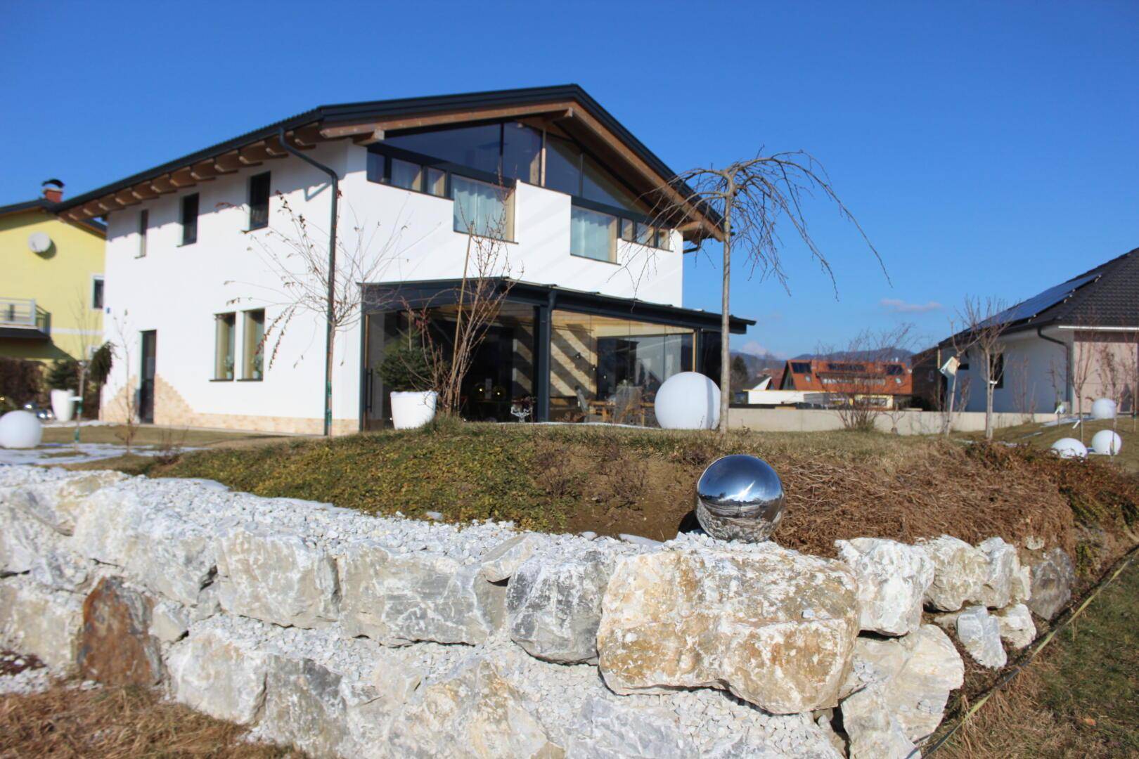 Ansicht des modernen Hauses mit Steingartenmauer und gepflegtem Rasen unter blauem Himmel.