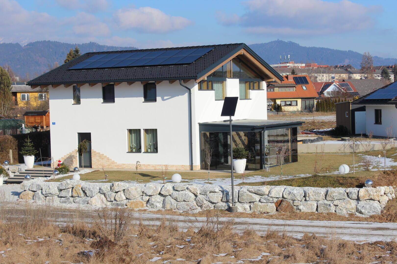Modernes Einfamilienhaus mit Photovoltaikanlage auf dem Dach und Wintergarten in ländlicher Umgebung.