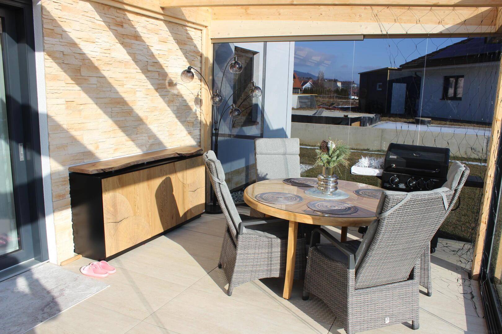 Gemütlicher Wintergarten mit Essbereich, Grill und dekorativer Steinwand, ideal für entspannte Stunden.