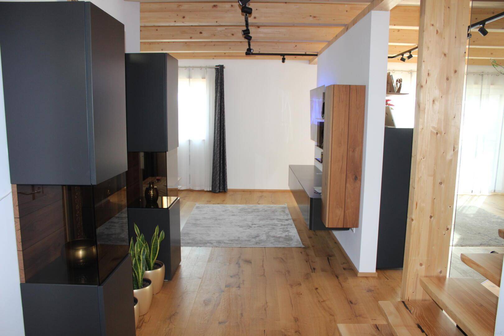 Geräumiger Wohnbereich mit Holzboden, sichtbaren Holzbalken und moderner Einrichtung.