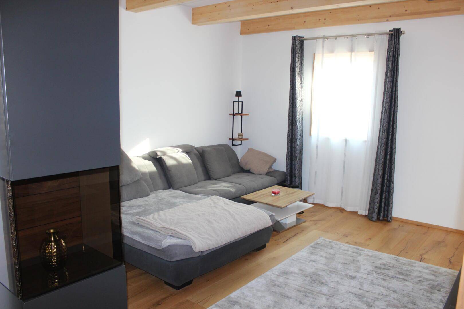 Gemütliches Wohnzimmer mit großem Sofa, Holzboden und viel Tageslicht durch das Fenster.