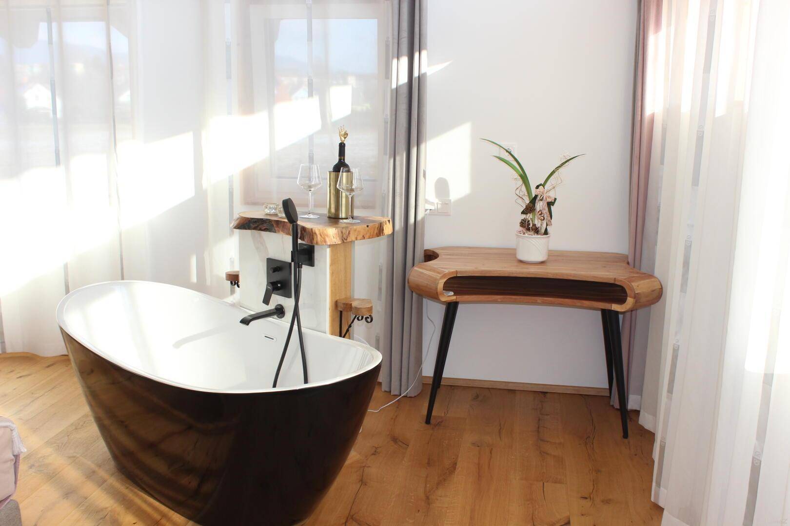 Elegante freistehende Badewanne im Schlafzimmer, umgeben von hellen Fenstern und Holzelementen.