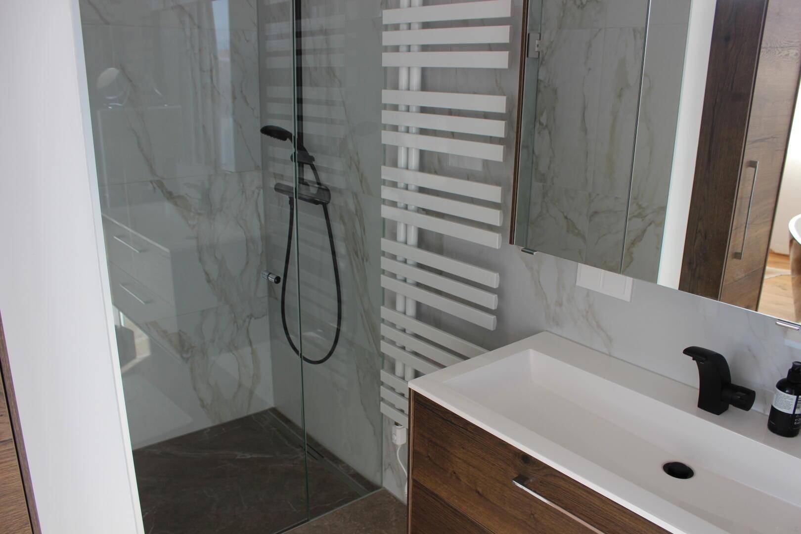 Modernes Badezimmer mit begehbarer Dusche, Waschtisch und eleganten Marmorfliesen.