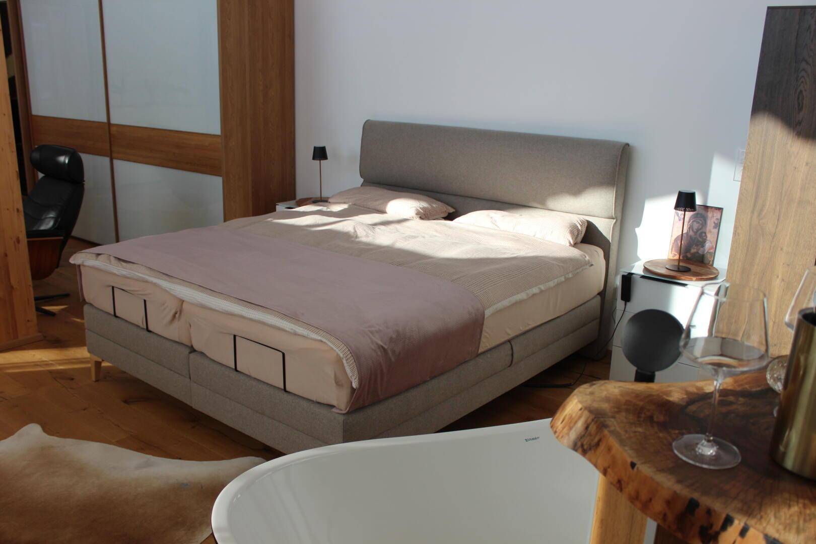 Komfortables Doppelbett in einem sonnigen Schlafzimmer mit Holzboden und moderner Einrichtung.