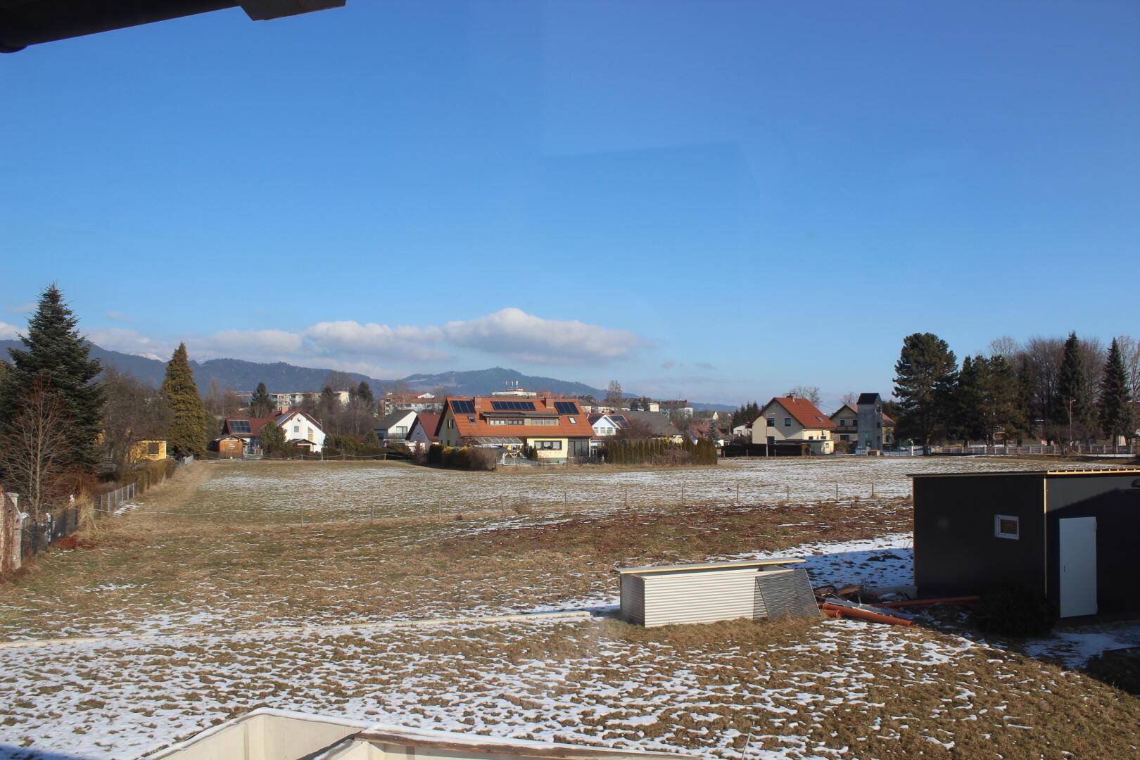 Weitläufiger Blick über Felder und Dächer der Nachbarschaft mit Bergen am Horizont.